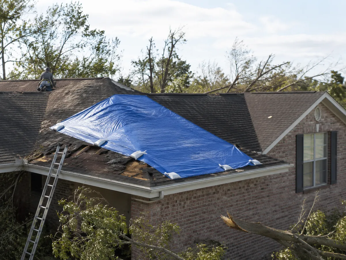 A storm-damaged roof with a blue tarp secured over missing shingles